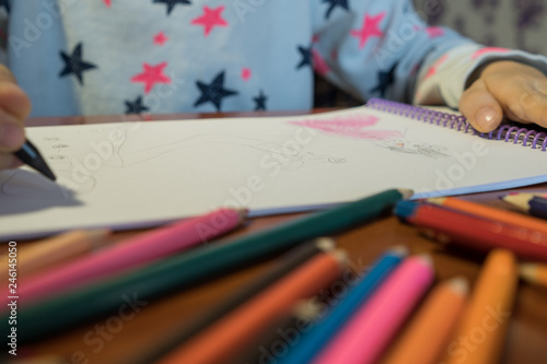 Colored pencils scattered on a wooden table. The child draws a picture in the album © semenenkostas