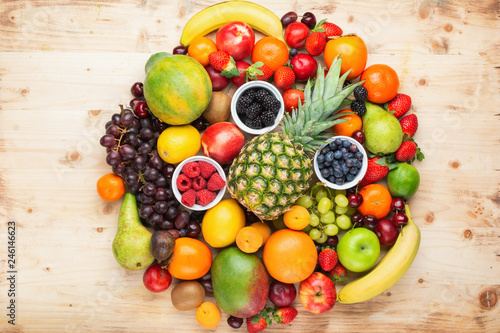Fototapeta Naklejka Na Ścianę i Meble -  Circle filled with healthy colorful fruits, strawberries raspberries oranges plums apples kiwis grapes blueberries mango persimmon on light wooden table, top view, copy space for text, selective focus