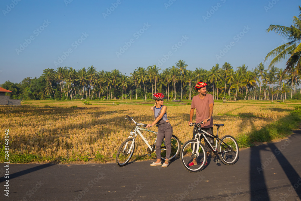 Happy young couple riding bicycles along road in summer. Leisure and lifestyle concept