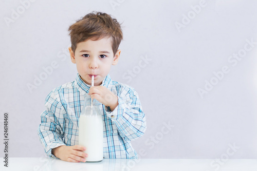 cute happy boy with dark eyes drinks milk from a bottle. the child is wearing a plaid shirt