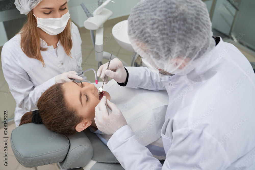 Dentist and assistant using restoration tools to client. Dentist and assistant using restoration tools to client.