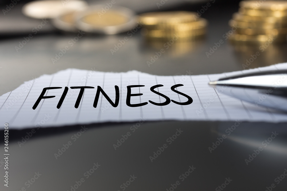 Fitness auf einem Zettel mit Stift vor Geldmünzen Fitness auf einem Zettel mit Stift vor Geldmünzen