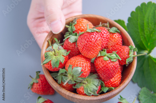 A young woman is holding a bowl of strawberries isolated on a airy blue background, closeup, topview, copyspace.