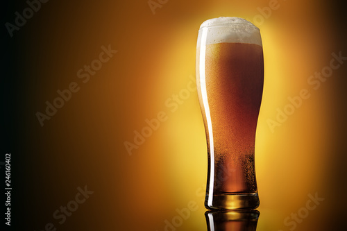 Glass just filled with fresh light lager beer on yellow to brown gradient background.