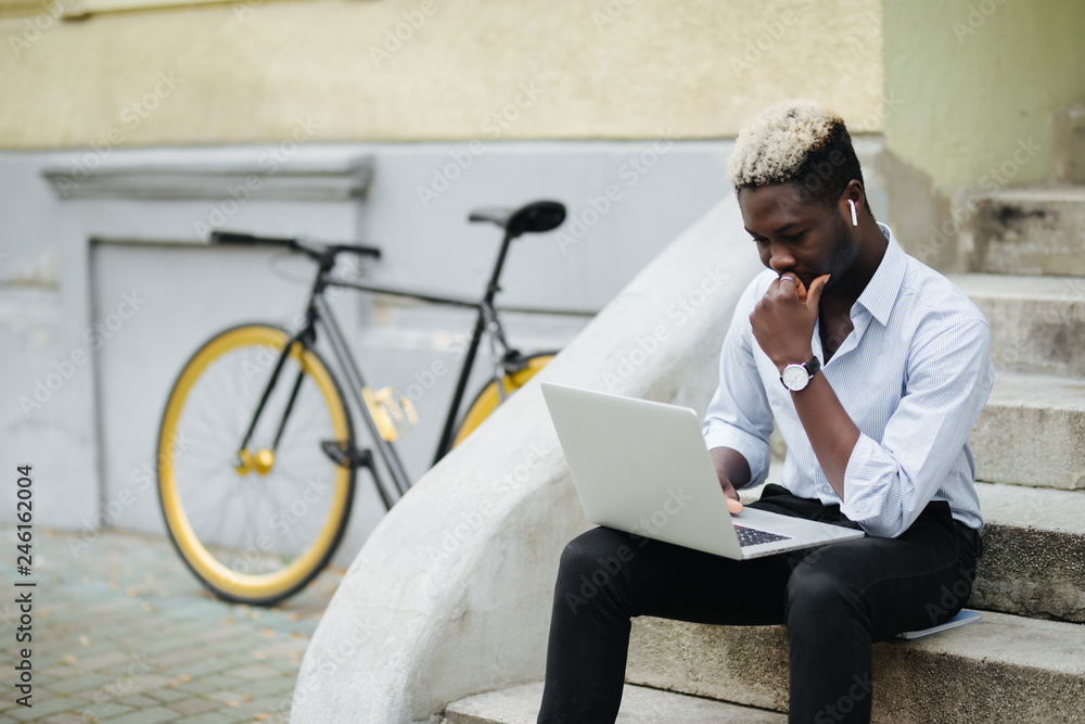 Stylish handsome african american freelancer working with laptop near bicycle in city Stylish handsome african american freelancer working with laptop near bicycle in city
