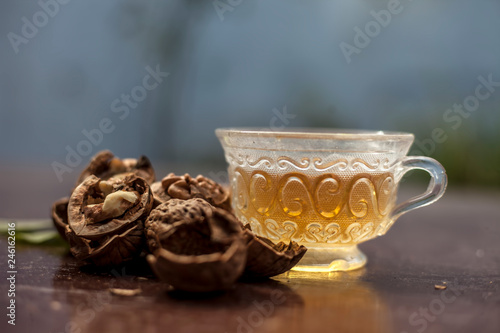 Close up of herbal organic tea of wall nut or walnut tea in a transparent glass cup with raw wall nut in shell and broken also. photo