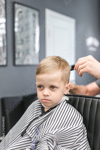 Barber cutting little boy blue-eyed blonde with hair clippers hair vertical photo