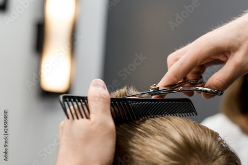 Barber cuts the little blond boy with scissors and combs in the hair salon close-up