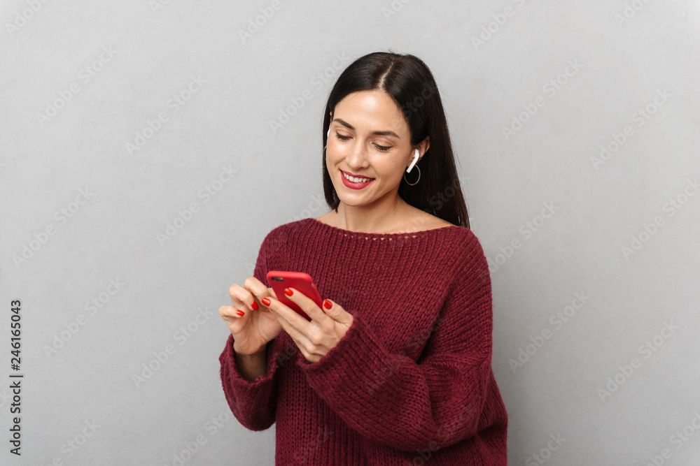 Pretty young woman dressed in burgundy sweater using mobile phone isolated over grey wall background. Pretty young woman dressed in burgundy sweater using mobile phone isolated over grey wall background.