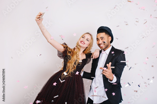 Amazing cute couple in love celebrating great party in tinsels, making selfie on white background. Luxury evening clothes, brightful positive emotions, Valentine s day, positivity, smiling