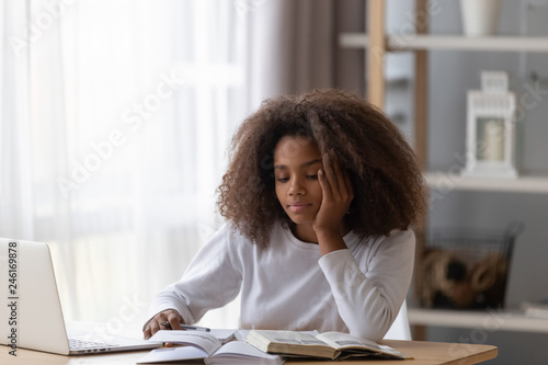 Tablou pe pânză Dreamy African American teenage girl sit at table with laptop and textbooks, dis