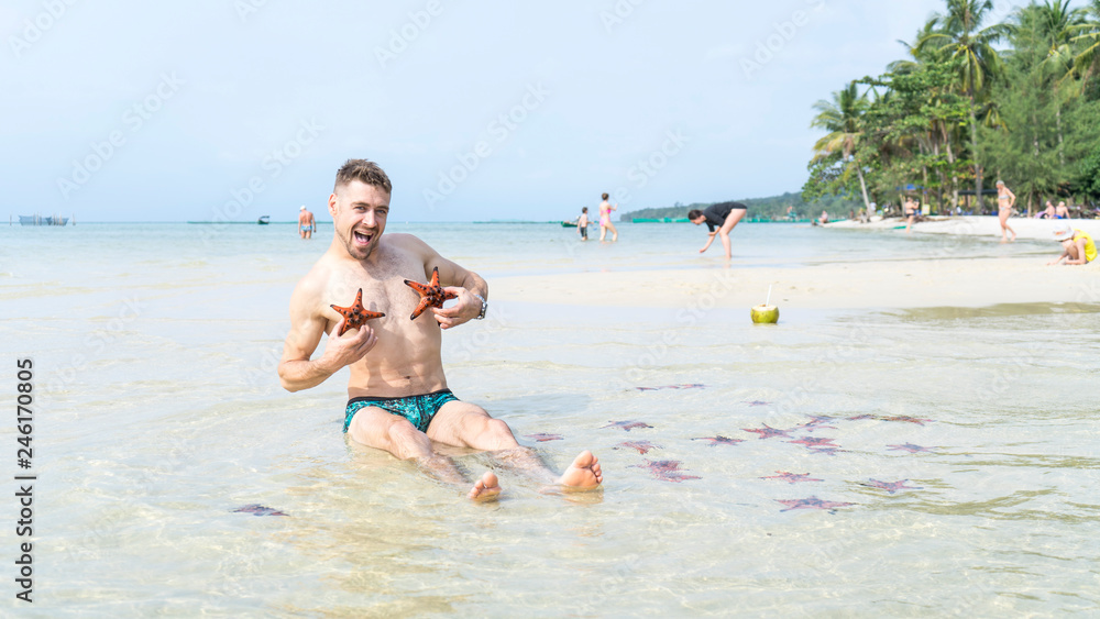 Travel boy is sitting on the sea with red starfishes makes funny photos in Phu Quoc island in crystal clear water