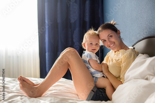 Young mother, sitting in bed with her baby boy, having shared moment of joy, breastfeeding, hugging, kissing, cudling © Tomsickova