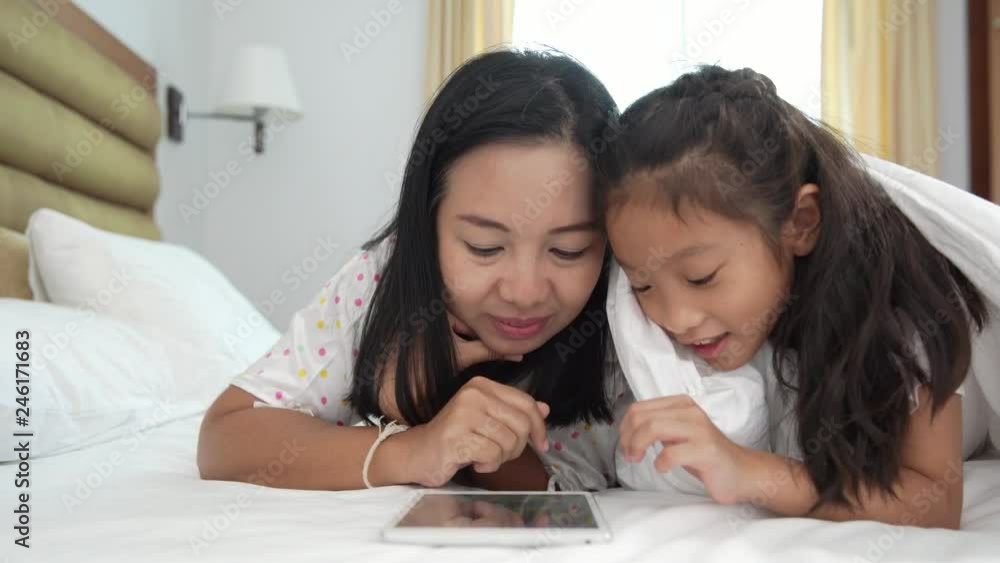 Mom and daughter playing smartphone on the bed, concept of social issue Mom and daughter playing smartphone on the bed, concept of social issue