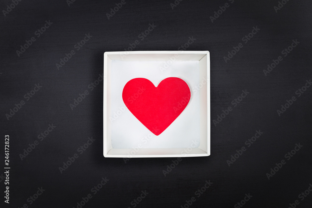 Red paper heart in white cardboard box on black chalkboard background. Flat lay. Top view. Valentine's Day concept