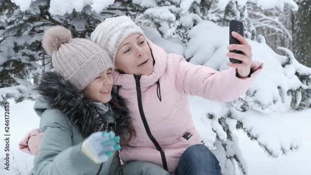 Happy family is photographed on the phone. Mother and child take pictures on a smartphone in the winter park. Happy family is photographed on the phone. Mother and child take pictures on a smartphone in the winter park.