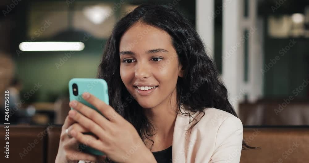 Business woman using app on smartphone sitting in modern office. Beautiful casual female professional in pink suit having good news on smartphone Business woman using app on smartphone sitting in modern office. Beautiful casual female professional in pink suit having good news on smartphone
