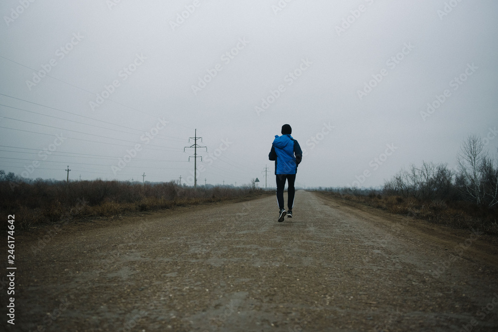 A man runs in headphones on the road. Stroke in pants and sneakers A man runs in headphones on the road. Stroke in pants and sneakers