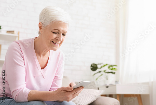 Cheerful aged woman using her smartphone at home