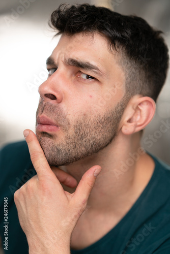 Handsome caucasian white male with black short hair and stubble with blue t shirt pondering