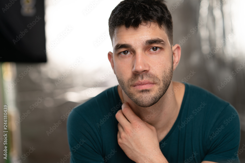 Handsome caucasian white male with black short hair and stubble with blue t shirt scratching his neck Handsome caucasian white male with black short hair and stubble with blue t shirt scratching his neck