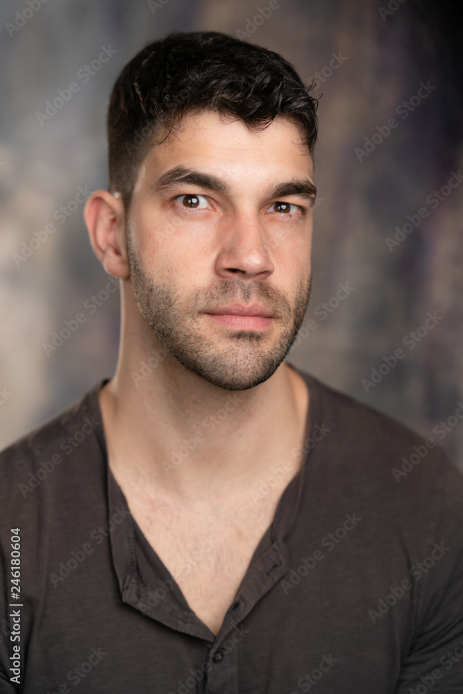 Obraz premium Handsome caucasian white male with black short hair and stubble with brown t shirt looking suspicious