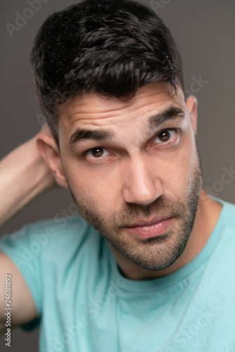 Handsome caucasian white male with black short hair and stubble with light blue t shirt, considering thinking