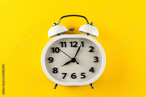 white vintage alarm clock on yellow background. - top view.