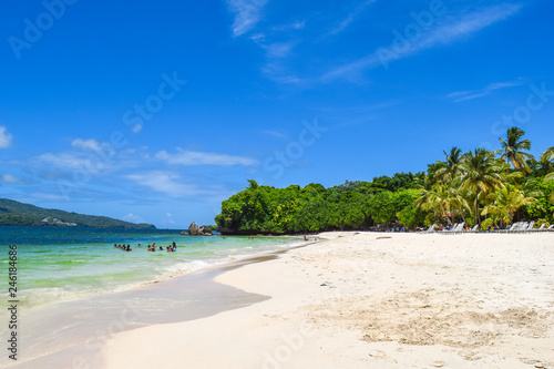 Tropical island in the caribbean sea with palms, white sand, turquoise ocean and blue sky, some tourists relaxing in the ocean and on the beach © Laila