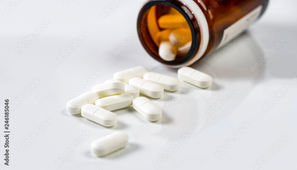 White medicine capsules scattered out of vial White medicine capsules scattered out of vial
