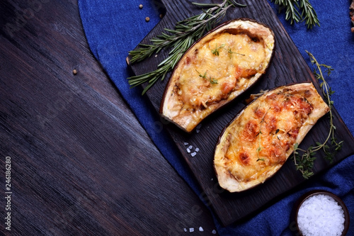 Stuffed eggplant halves roasted with cheese on a black cutting board