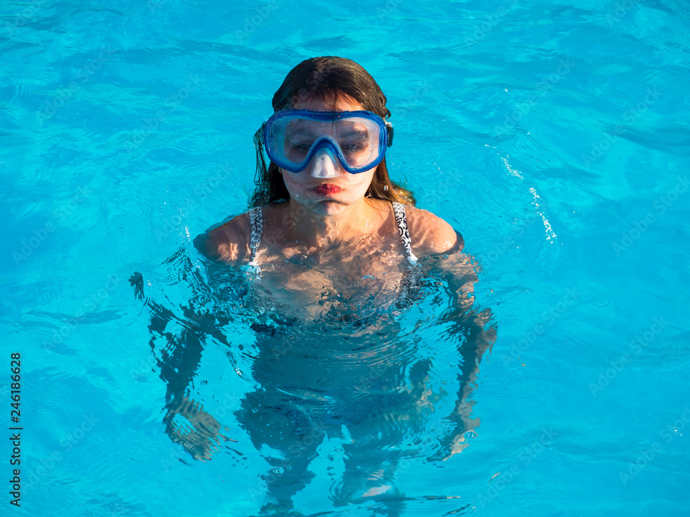 Naklejka premium Cute happy young girl in goggles swimming and snorking in the swimming pool