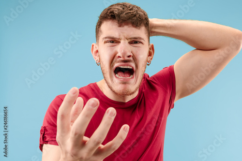 Screaming, hate, rage. Crying emotional angry man screaming on blue studio background. Emotional, young face. male half-length portrait. Human emotions, facial expression concept. Trendy colors