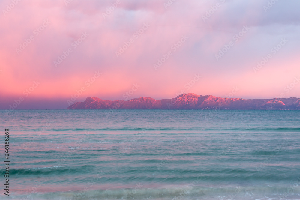 Rosaroter Himmel über den Bergen am Horizont beim Sonnenuntergang am Meer