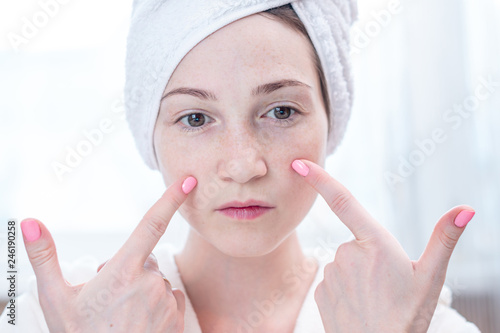Beautiful happy young woman with a towel on her head looking at her skin in a mirror. Hygiene and care for the skin