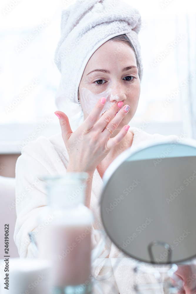 Beautiful happy young woman applying cream on face moisturizing the skin. Concept of hygiene and care for the skin Beautiful happy young woman applying cream on face moisturizing the skin. Concept of hygiene and care for the skin