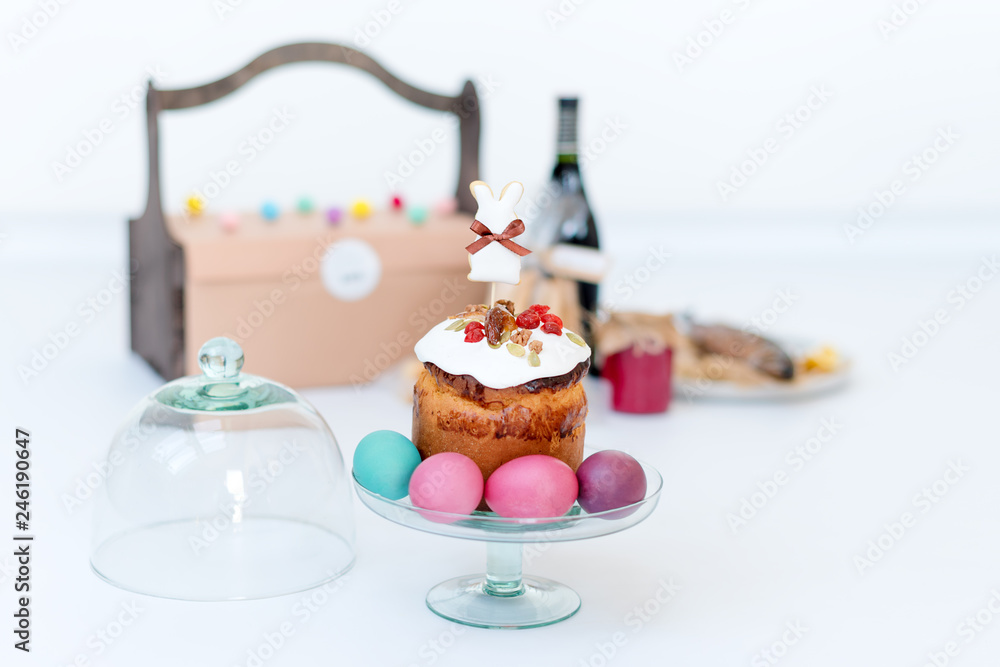 Easter cake, colored eggs and bottle of red wine. Easter composition with orthodox sweet bread, kulich and bottle of wine on light background. Gifts for holiday in wooden basket. Copyspace for text Easter cake, colored eggs and bottle of red wine. Easter composition with orthodox sweet bread, kulich and bottle of wine on light background. Gifts for holiday in wooden basket. Copyspace for text