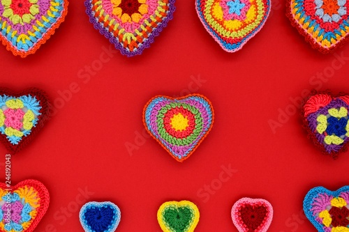 Knitted hearts of colored yarn on a red background. Valentine's Day, love, handmade, amigurumi, hobby, decoration, postcard, creative.