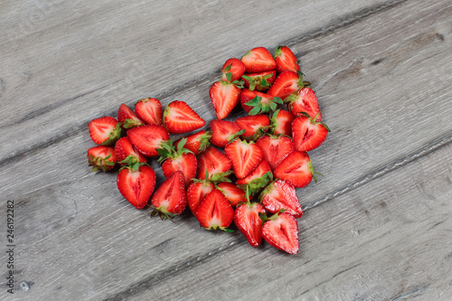 Strawberries cut in half, arranged to shape of heart, placed on gray wood desk.