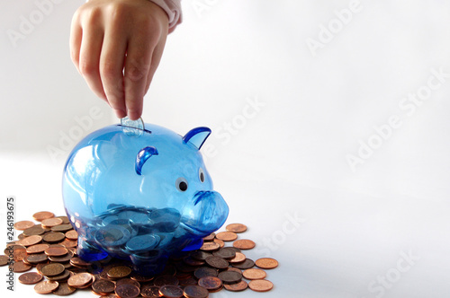 Wallpaper Mural Child`s hand putting money in blue transparent piggy bank on pennies with copy space Torontodigital.ca