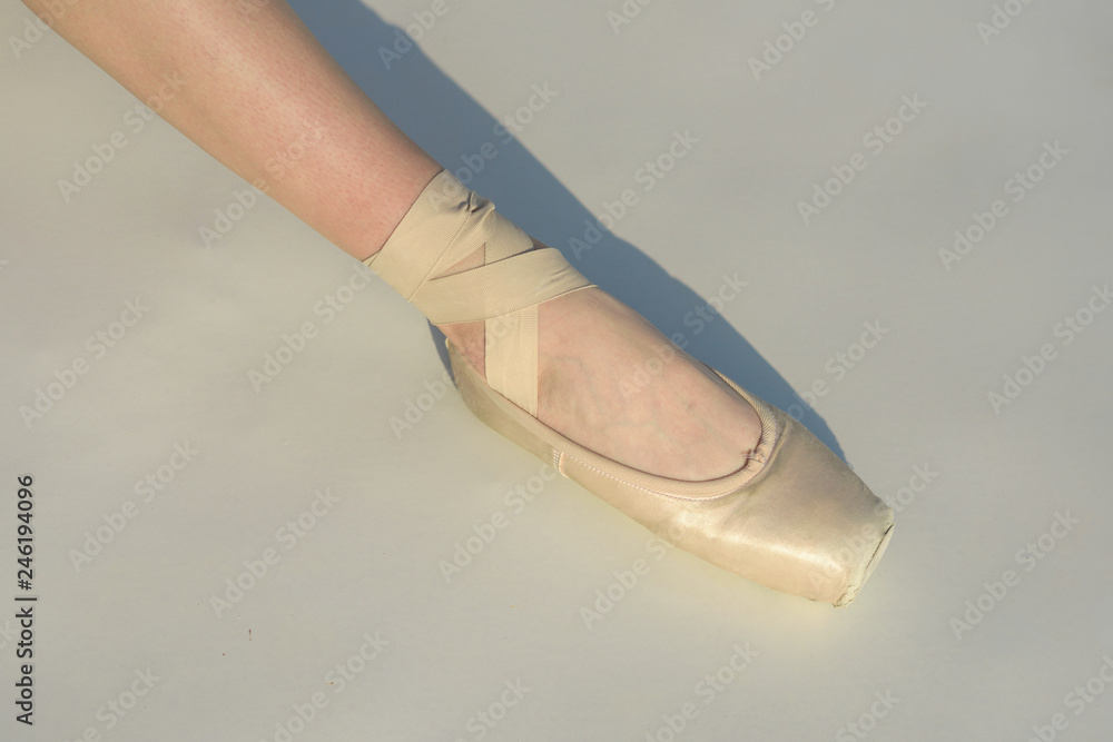 Toe dancing. Ballerina leg in white ballet shoe. Lacing ballet slipper. Female foott in pointe