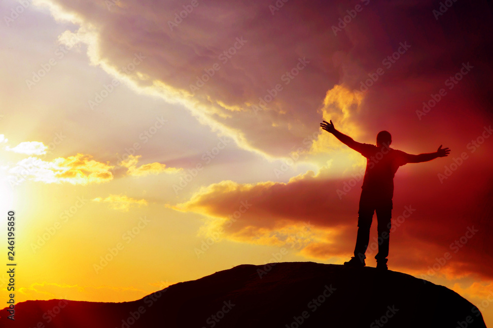silhouette of a man on top of a mountain with his hands up at sunset. achieving goal.