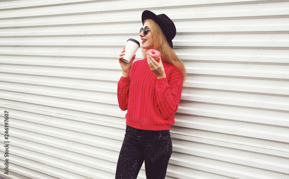 Portrait happy young woman drinks coffee and holding sweet donut on city street white wall background