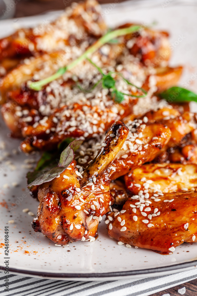 American cuisine concept. Fried glazed chicken legs with sesame on a white plate with chilli peppers. Background image for a menu in restaurants or cafes. copy space American cuisine concept. Fried glazed chicken legs with sesame on a white plate with chilli peppers. Background image for a menu in restaurants or cafes. copy space