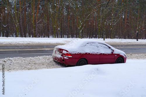 View of the car in the snow near the asphalt and in the distance of the forest in winter.