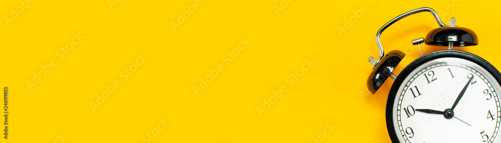 Black retro alarm clock on yellow background top view Flat lay copy space. Minimalistic background, concept of time, deadline, time to work, morning