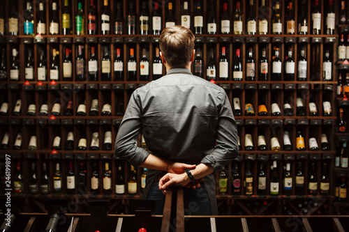 Bartender at wine cellar full of bottles with exquisite drinks photo