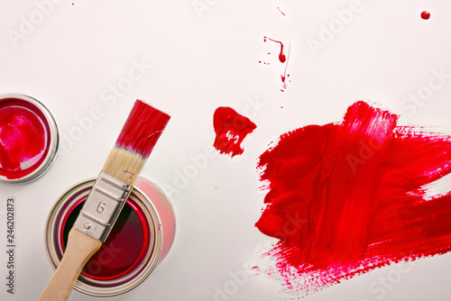 Open red paint canister on white table painted with brush