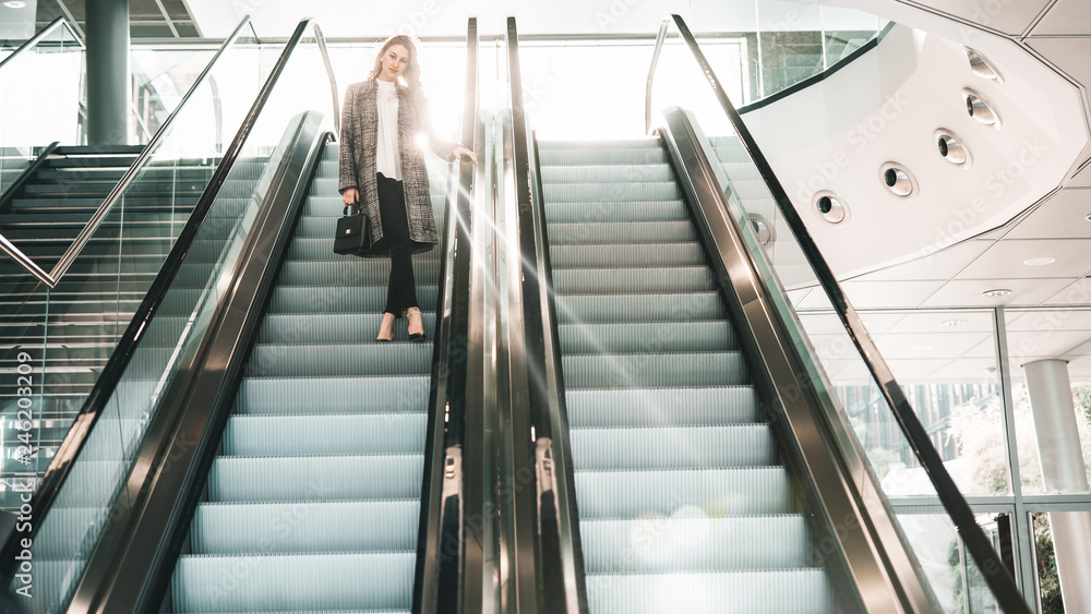 Obraz premium Hübsche junge Frau im Sonnenlicht auf einer Rolltreppe posing lifestyle bokeh