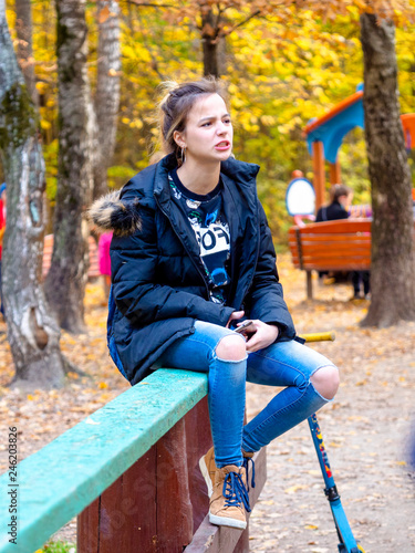 Charming grimacing girl in the autumn forest. Portrait of a teenager sitting on a wooden railing in an autumn park on a sunny day. photo